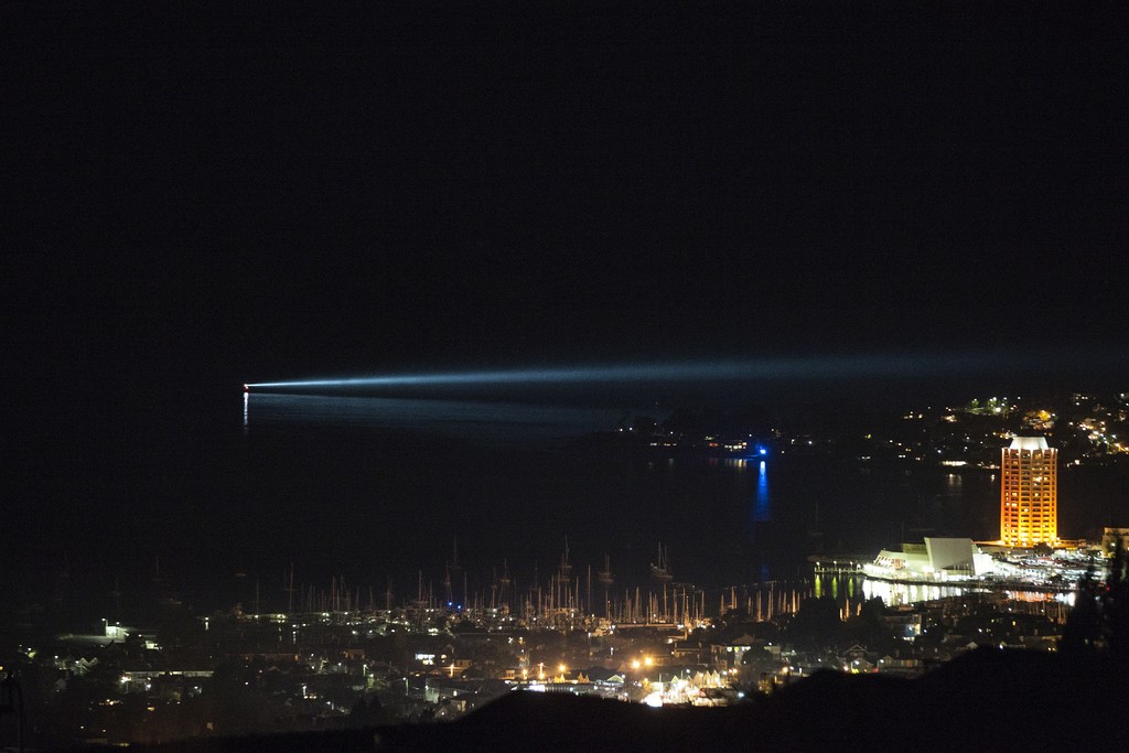 Anthony McCall,
Night Ship, 2015,
A unique commission especially for Dark Mofo, 2015.
A dark ship sails nightly from Tinderbox to Mona via the city’s harbour. At regular intervals, a powerful pencil-slim searchlight radiates from the vessel to illuminate the adjacent shore.
Photo credit: MONA/Rémi Chauvin
Image Courtesy of MONA (Museum of Old and New Art) Anthony McCall,
Night Ship, 2015,
A unique commission especially for Dark Mofo, 2015.
A dark ship sails nightly from Tinderbox to Mona via the city’s harbour. At regular intervals, a powerful pencil-slim searchlight radiates from the vessel to illuminate the adjacent shore.
Photo credit: MONA/Rémi Chauvin
Image Courtesy of MONA (Museum of Old and New Art)