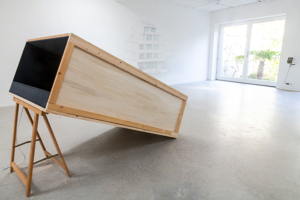 exhibition view: „There and Back“ (front), 2014 | Video, HD, loop, with audio, projection in box, collaboration with Mario Marchisella – From the series: „lost monuments, No. 1“ (back left), 2015 | staged after a found image of a nail house in China, drawing with colored pencils directly onto the wall of the exhibition space, ca. 2 x 3m – „There is no place like home“ (back right), 2012 | wooden object, digital frame with text animation, 16, 5 x 12 x 9,5cm | image: ©dasesszimmer exhibition view: „There and Back“ (front), 2014 | Video, HD, loop, with audio, projection in box, collaboration with Mario Marchisella – From the series: „lost monuments, No. 1“ (back left), 2015 | staged after a found image of a nail house in China, drawing with colored pencils directly onto the wall of the exhibition space, ca. 2 x 3m – „There is no place like home“ (back right), 2012 | wooden object, digital frame with text animation, 16, 5 x 12 x 9,5cm | image: ©dasesszimmer