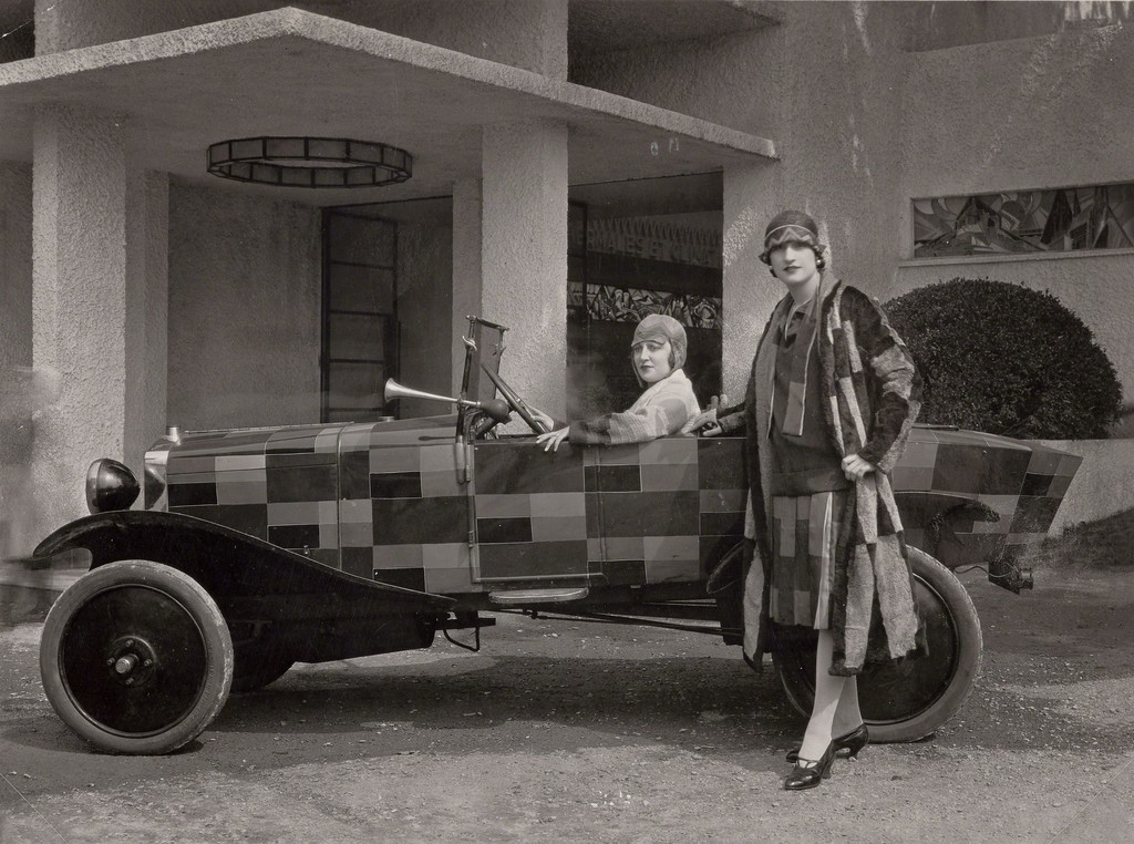 Two models wearing fur coats designed by Sonia Delaunay and manufactured by Heim, with the car belonging to the journalist Kaplan and painted after one of Sonia Delaunay’s fabrics, in front of the Pavillon du Tourisme designed by Mallet-Stevens, International Exposition of Modern Industrial and Decorative Arts, Paris 1925.
Bibliothèque nationale de France, Paris. Courtesy Tate Modern. Two models wearing fur coats designed by Sonia Delaunay and manufactured by Heim, with the car belonging to the journalist Kaplan and painted after one of Sonia Delaunay’s fabrics, in front of the Pavillon du Tourisme designed by Mallet-Stevens, International Exposition of Modern Industrial and Decorative Arts, Paris 1925.
Bibliothèque nationale de France, Paris. Courtesy Tate Modern.