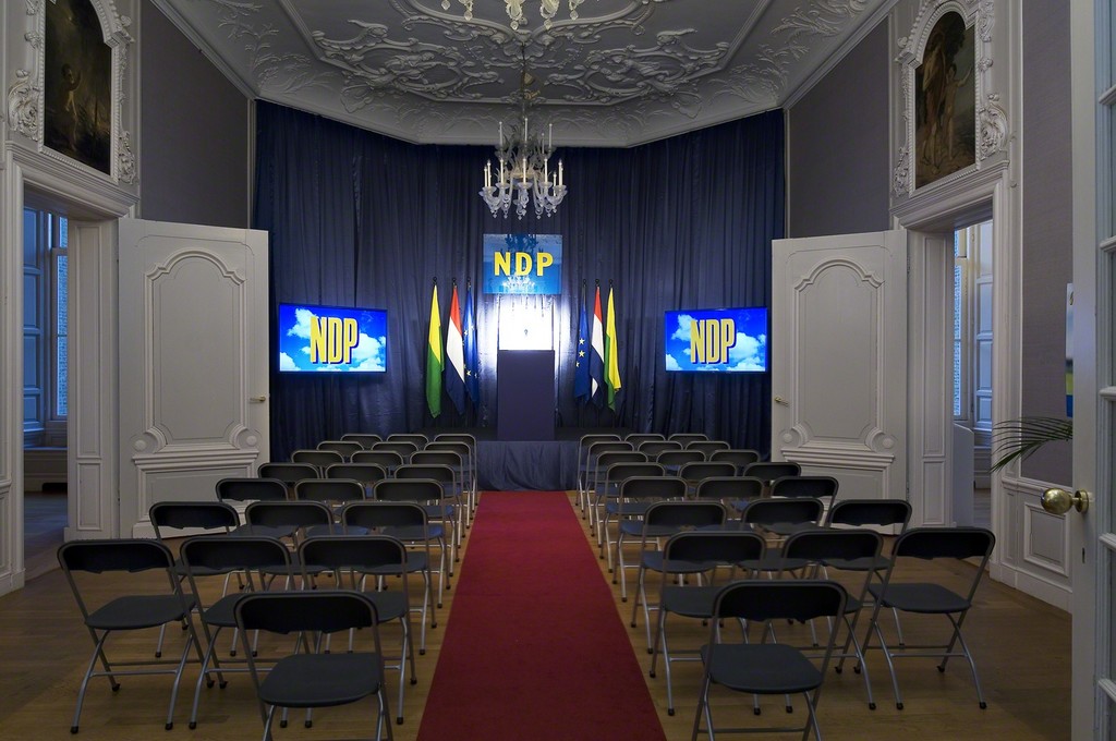 Guillaume Bijl. Nieuwe Demokratische Partij (A New Democratic Party). Installation with chairs, stage, flatscreens, flags, palms, lights, music, curtain, posters, pulpit etc, 2016. 500 x 800 x 1100 cm
Guillaume Bijl. Nieuwe Demokratische Partij (A New Democratic Party). Installation with chairs, stage, flatscreens, flags, palms, lights, music, curtain, posters, pulpit etc, 2016. 500 x 800 x 1100 cm