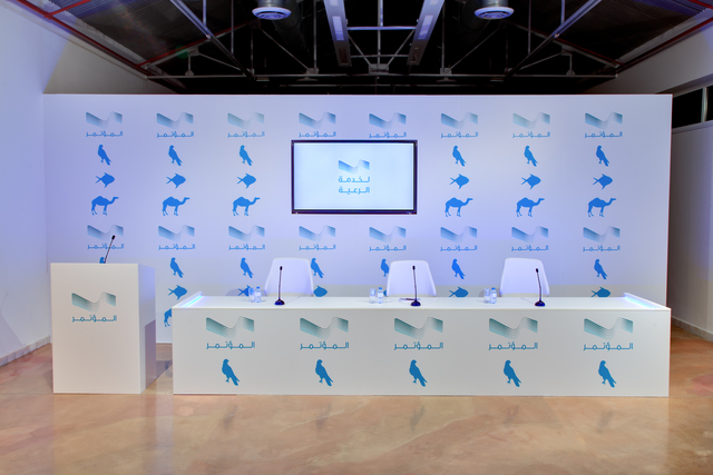 GCC, ‘Mu'tamar | Press Conference’, 2015, Installation, Wood, vinyl, HD video, chairs, glasses, water bottles, podium microphones, Project Native Informant