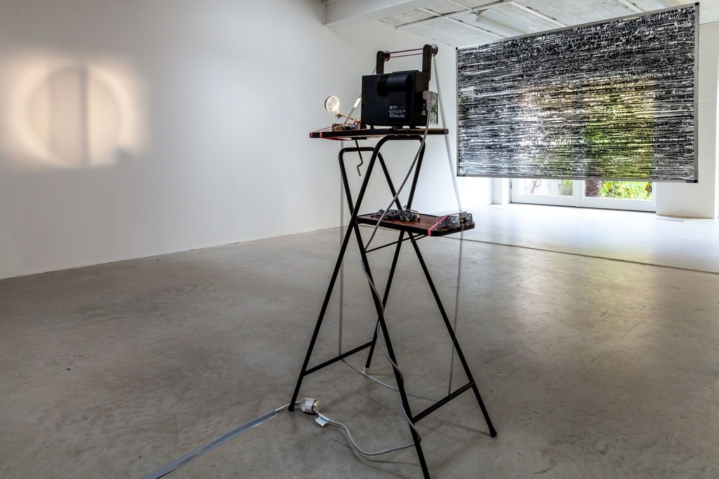 Jens Standke, exhibition view: (foreground) „Visual Loops“, 2016 | videotapelLoop, film projector, magnifying glas, rubber bands, projector table and (background) „On/Off: X-Files“, 2016 | videotape, tape, aluminium, 210 x 130cm | image: ©dasesszimmer Jens Standke, exhibition view: (foreground) „Visual Loops“, 2016 | videotapelLoop, film projector, magnifying glas, rubber bands, projector table and (background) „On/Off: X-Files“, 2016 | videotape, tape, aluminium, 210 x 130cm | image: ©dasesszimmer