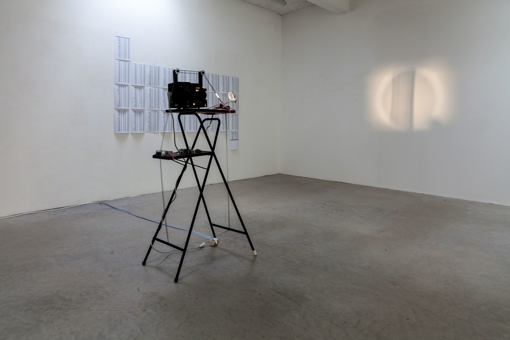 Jens Standke, exhibition view: (foreground) „Visual Loops“, 2016 | videotape, Loop, film projector, magnifying glas, rubber bands, projector table and (background) „2,339 cm/s“, 2016 | s/w laser print on A4 paper, 32 pages, format variable | image: ©dasesszimmer Jens Standke, exhibition view: (foreground) „Visual Loops“, 2016 | videotape, Loop, film projector, magnifying glas, rubber bands, projector table and (background) „2,339 cm/s“, 2016 | s/w laser print on A4 paper, 32 pages, format variable | image: ©dasesszimmer