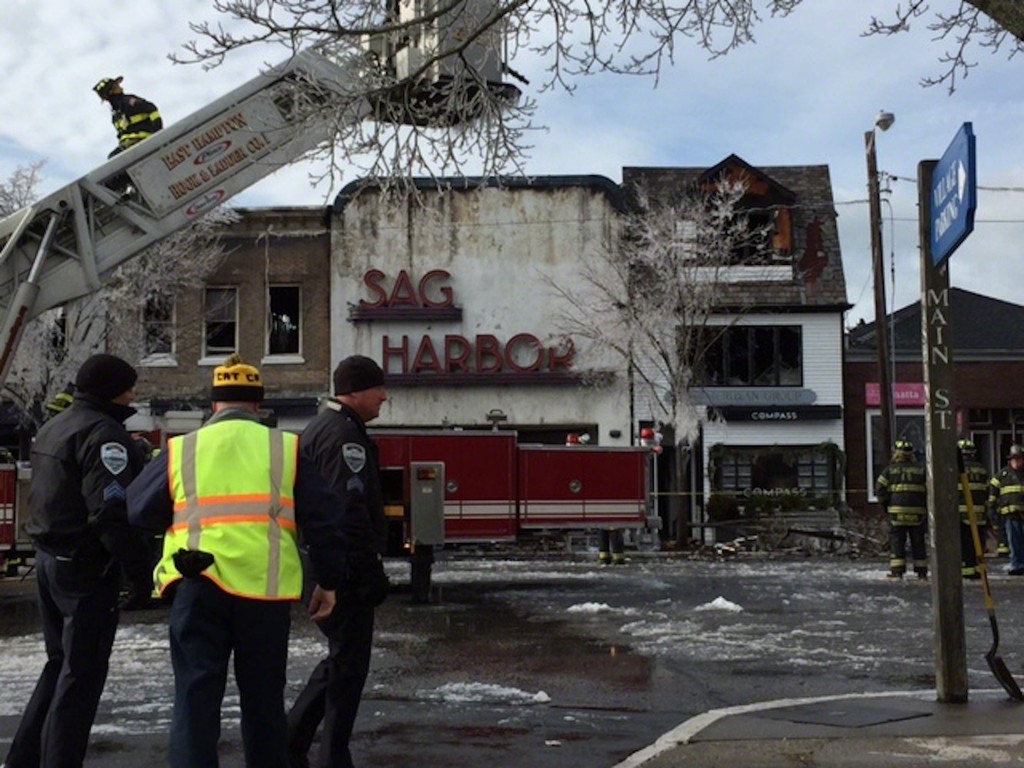 12/16/2016 - Sag Harbor First Responders have finally stopped the fire. A tree in the background is frozen from water from the fire hoses. The burnt cinema facade stands. 12/16/2016 - Sag Harbor First Responders have finally stopped the fire. A tree in the background is frozen from water from the fire hoses. The burnt cinema facade stands.