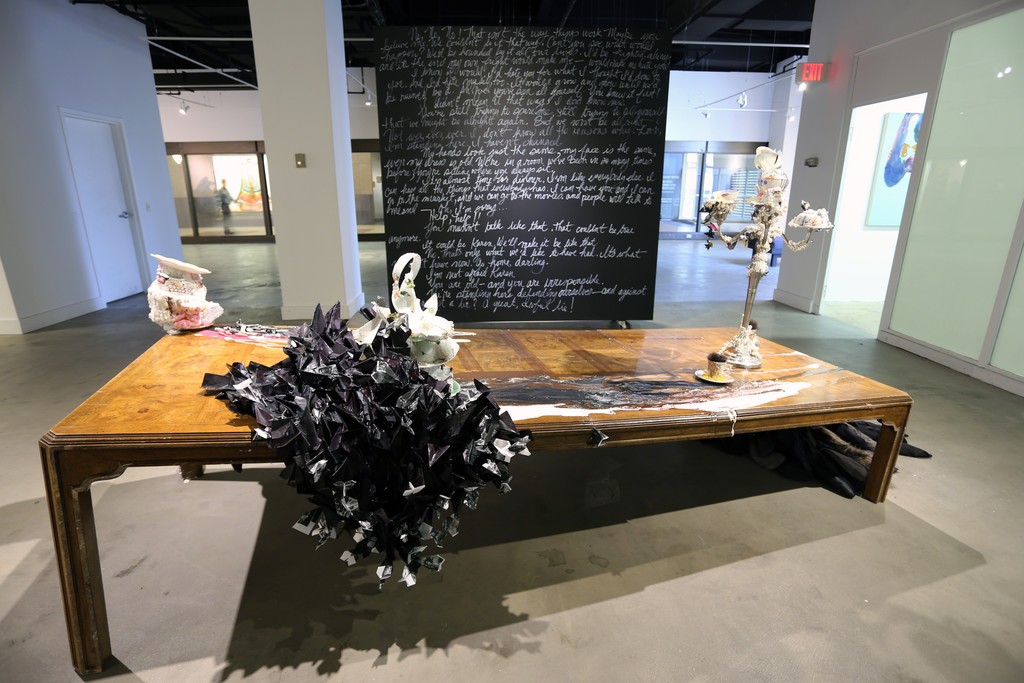 The black wall features text from the performance piece by David Antonio Cruz, greenhowiwantyou, green. Installation of a broken table with paint, paper with resin, sculpture and costumes pieces from past performances. The black wall features text from the performance piece by David Antonio Cruz, greenhowiwantyou, green. Installation of a broken table with paint, paper with resin, sculpture and costumes pieces from past performances.