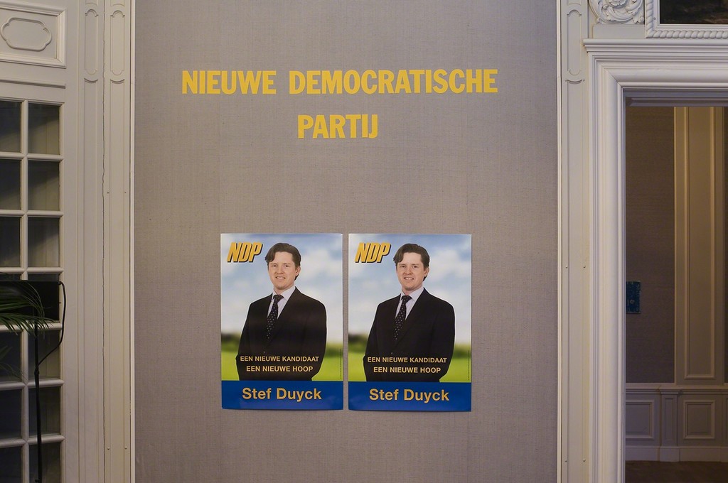 Guillaume Bijl. Nieuwe Demokratische Partij (A New Democratic Party). Installation with chairs, stage, flatscreens, flags, palms, lights, music, curtain, posters, pulpit etc, 2016. 500 x 800 x 1100 cm. Detail Guillaume Bijl. Nieuwe Demokratische Partij (A New Democratic Party). Installation with chairs, stage, flatscreens, flags, palms, lights, music, curtain, posters, pulpit etc, 2016. 500 x 800 x 1100 cm. Detail