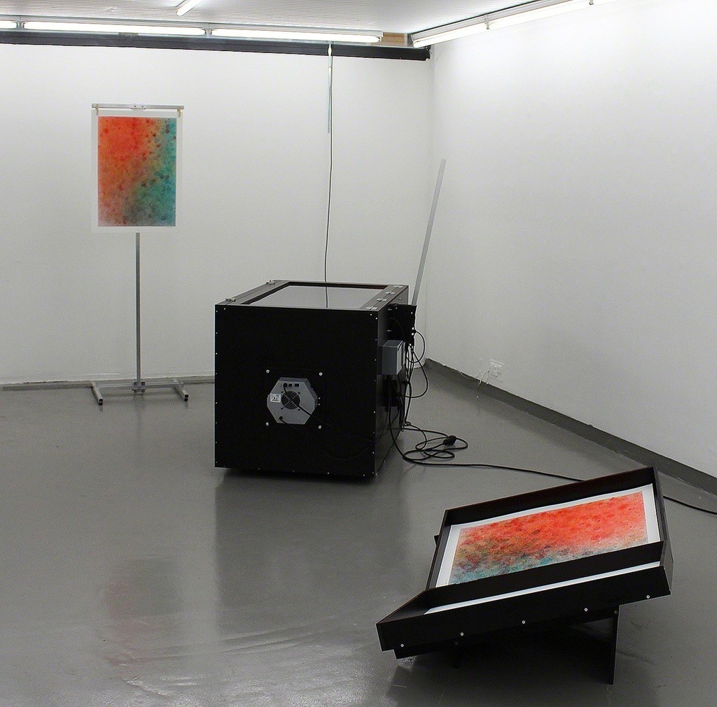 SB007 Watercolour Tool (Installation), 2016, Panels, electronics, paper and soap, 160 x 90 x 135 cm. With help from soap bubbles SB007 paints watercolors in red, yellow and blue. The colour of the soapwater is controlled by the daylight, and the colour is blown out in bubbles bursting on the paper consequently leaving a mark. Slowly the day appears on the paper. Aware of its own nature-romantic tradition the SB007 works with the ’special’ Nordic light as a catalyst of the artistic process. SB007 Watercolour Tool (Installation), 2016, Panels, electronics, paper and soap, 160 x 90 x 135 cm. With help from soap bubbles SB007 paints watercolors in red, yellow and blue. The colour of the soapwater is controlled by the daylight, and the colour is blown out in bubbles bursting on the paper consequently leaving a mark. Slowly the day appears on the paper. Aware of its own nature-romantic tradition the SB007 works with the ’special’ Nordic light as a catalyst of the artistic process.