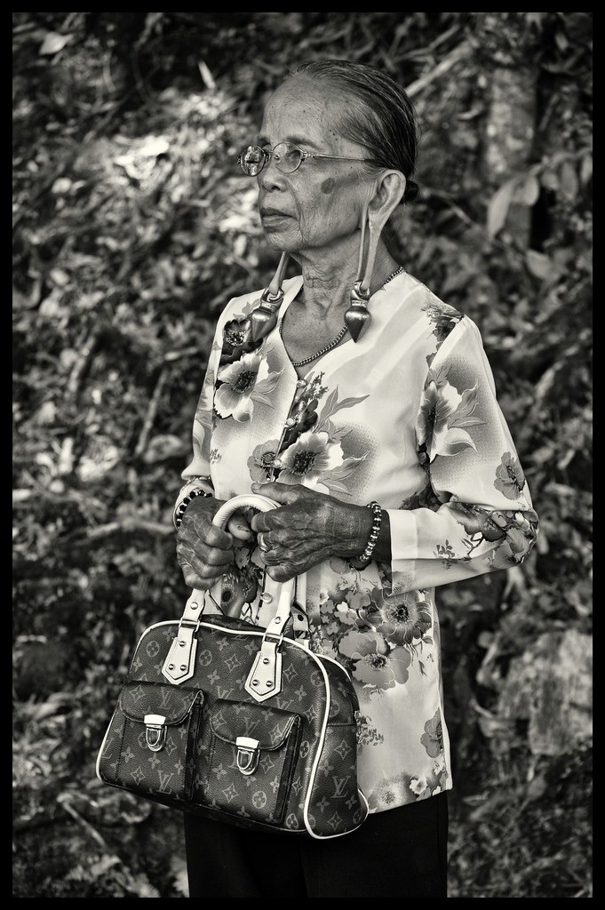 This Kayan women is from Upper Baram River in Long Miri. Her ear lobes are distended by heavy brass rings.
Why is this image important?
It epitomizes the idea of change where there is no conflict between traditional values (wearing the brass ear rings) and carrying a modern LV handbag. Her tattooed hands also tell you of her aristocratic background. This Kayan women is from Upper Baram River in Long Miri. Her ear lobes are distended by heavy brass rings.
Why is this image important?
It epitomizes the idea of change where there is no conflict between traditional values (wearing the brass ear rings) and carrying a modern LV handbag. Her tattooed hands also tell you of her aristocratic background.
