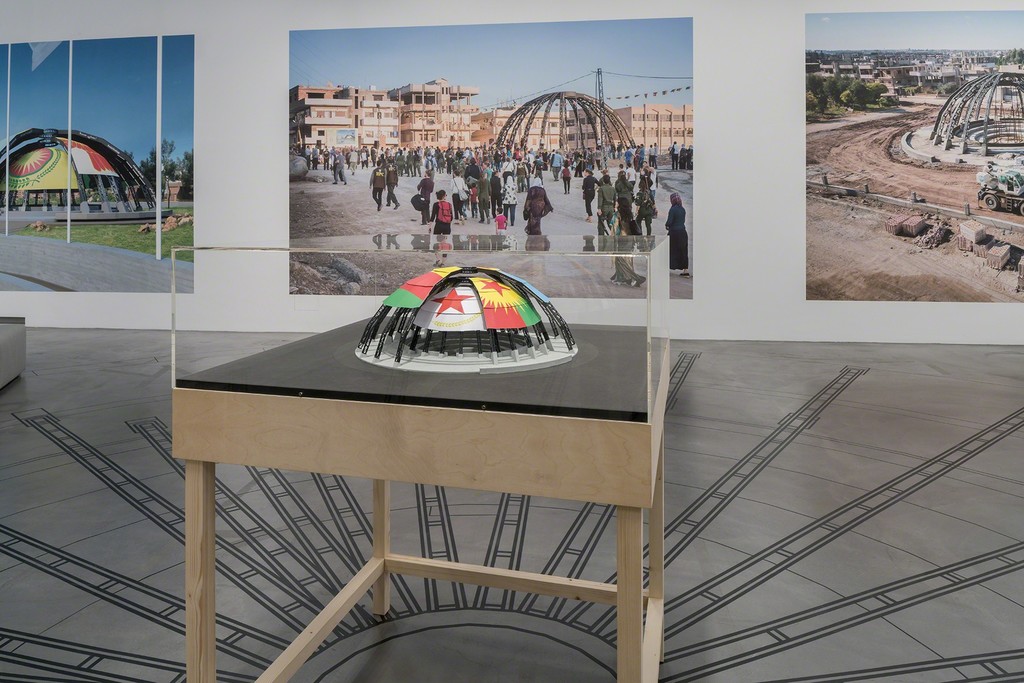 Democratic Self-Administration of Rojava and Studio Jonas Staal, New World Summit – Rojava, 2015–
2017, Architectural model, single-channel video, projection (color, sound), single-channel video on monitor
(color, sound), adhesive PVC foil, digital print, acrylic on paper, dimensions variable, Sammlung Migros
Museum für Gegenwartskunst
Exhibition view Migros Museum für Gegenwartskunst, photo: Lorenzo Pusterla Democratic Self-Administration of Rojava and Studio Jonas Staal, New World Summit – Rojava, 2015–
2017, Architectural model, single-channel video, projection (color, sound), single-channel video on monitor
(color, sound), adhesive PVC foil, digital print, acrylic on paper, dimensions variable, Sammlung Migros
Museum für Gegenwartskunst
Exhibition view Migros Museum für Gegenwartskunst, photo: Lorenzo Pusterla